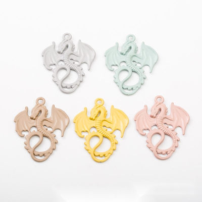 Curled winged dragon charms with smooth pastel coatings arranged together on a white background.