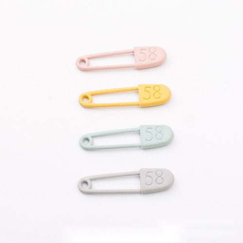 Slender safety pin with a rounded numbered cover shown in the available finishes