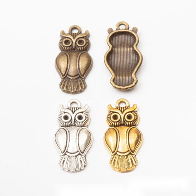 Product view of long owl pendant showing a long owl with round eyes, recessed wing panels, tail feathers, and a top loop