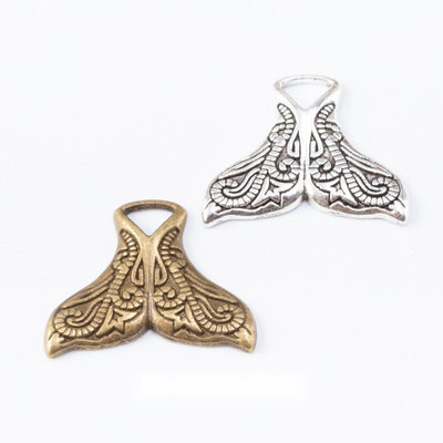 Whale-tail charms with engraved swirling linework arranged together on a white background.
