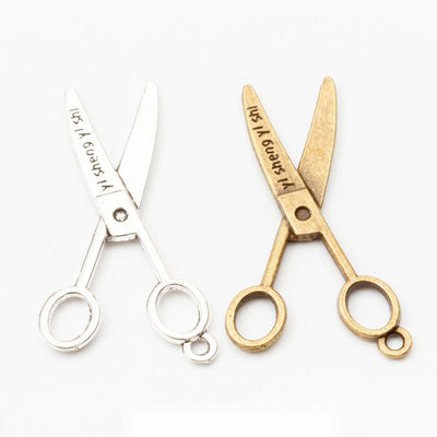 Product photo 1 of the vintage scissors charm highlighting its open scissors silhouette with engraved script on one blad
