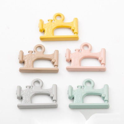 Mini sewing machine charms with smooth pastel coatings arranged together on a white background.