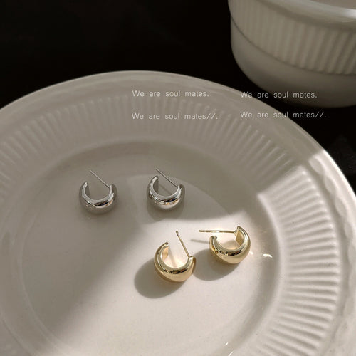 Polished chunky C-shaped stud earrings shown together on a white plate.