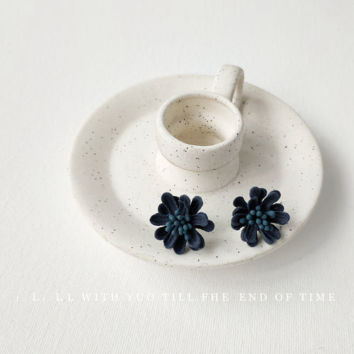Dusty blue fabric flower studs on white canvas close-up