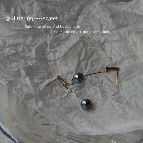 Gold bar black pearl drop earrings on crumpled white paper
