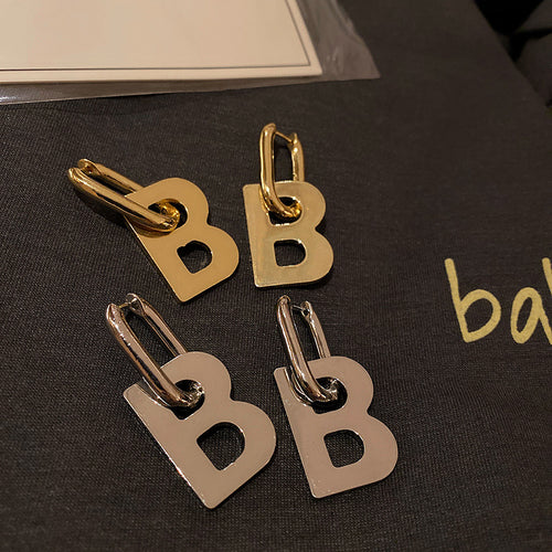 Gold and silver letter B hoop earring pairs on dark fabric