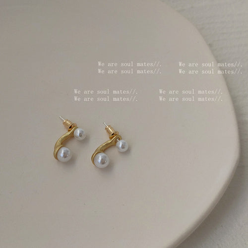 Pair of matte gold pearl arc studs on white fabric