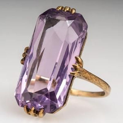 Gold tone large rectangular purple stone ring on light surface