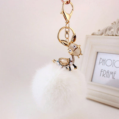 White fluffy pom pom beneath a gold-tone donkey charm and key hardware.