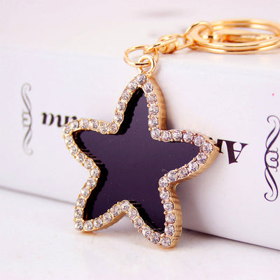 Close-up of a black five-point star with clear rhinestone edging attached to a gold-tone split key ring.