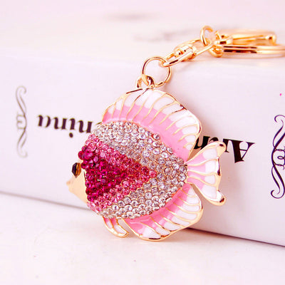Close-up of a pink rhinestone fish keychain resting against a white box.
