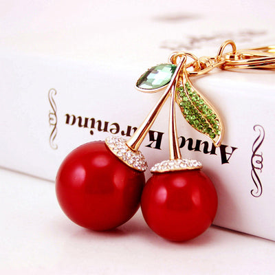 Close-up of two glossy red cherry charms with green leaves and clear rhinestone accents.