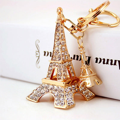 Close-up of a rhinestone-covered Eiffel Tower charm beside a smaller tower charm and gold-tone key hardware.