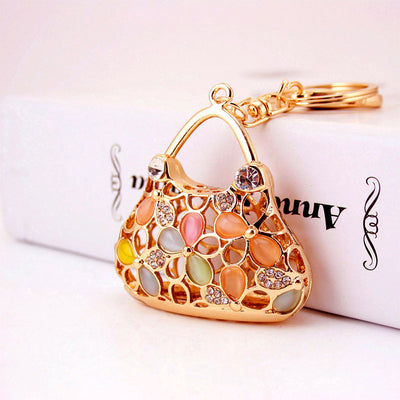Front view of a gold-tone handbag charm with multicolor floral inlays beside a white box.