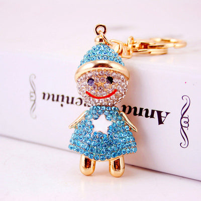 A blue rhinestone doll charm is shown close up with gold-tone limbs and a smiling face.