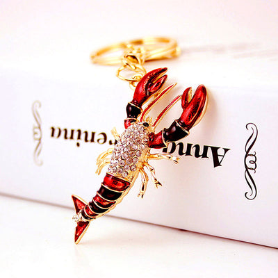 A red and black rhinestone lobster charm hanging from a gold-tone split ring.