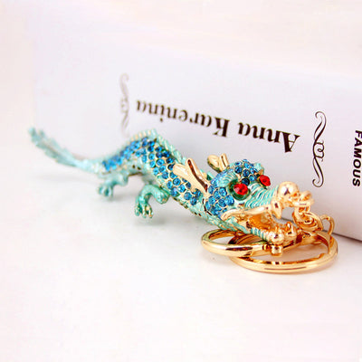 Aqua-blue rhinestone dragon resting beside its gold-tone split ring.