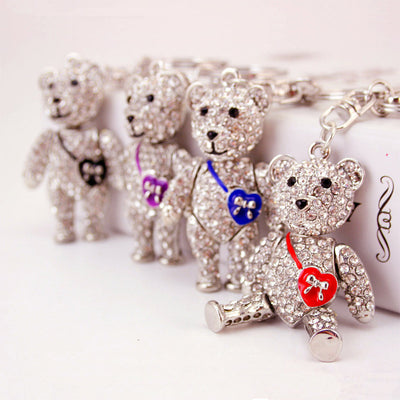 Four clear-stone teddy bear keychains with red, blue, purple, and black heart charms arranged together.