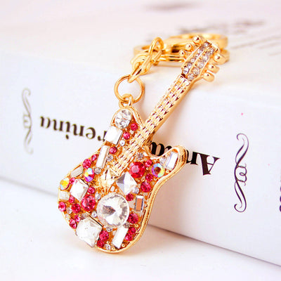 Close-up of a pink rhinestone guitar charm attached to a gold-tone key ring.