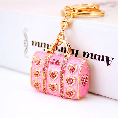Angled close-up of a pink handbag keychain with pink heart accents and gold-tone hardware.