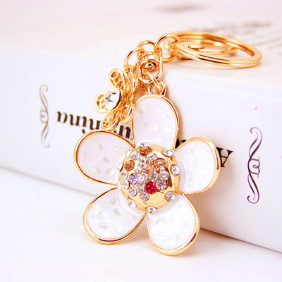 Close-up of a white five-petal charm with clear, champagne, and red stones beside a split key ring.