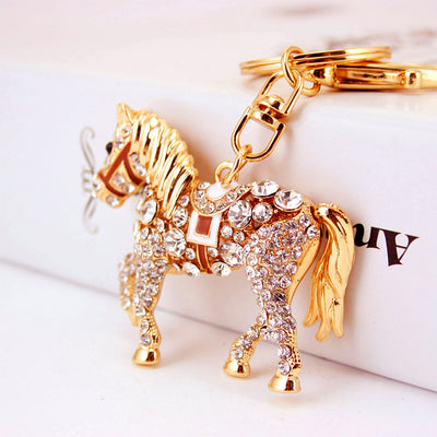 Close side view of a gold tone rhinestone horse keychain beside a white box.