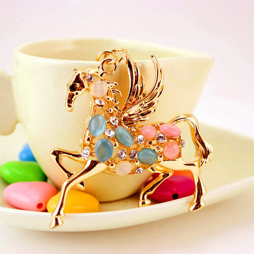 Gold-tone winged horse figure displayed against a yellow cup and colorful beads.