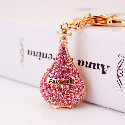 Pink rhinestone perfume bottle charm attached to gold-tone keychain hardware.