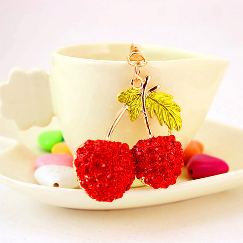 Red double-cherry charm hanging in front of a cream cup and saucer.