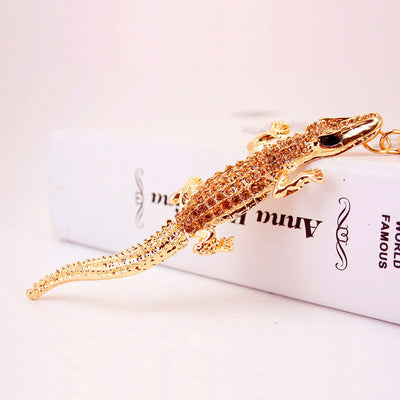 Angled view of a gold-tone crocodile accessory covered with brown rhinestones on a white box.