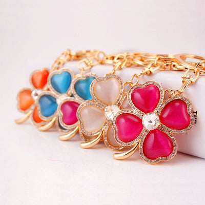 Several gold-tone clover keychains in pink, white, blue, and orange arranged in a row.