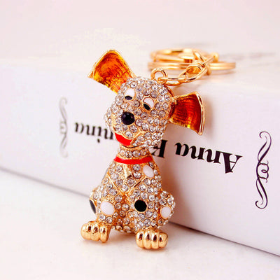 Gold-tone spotted dog pendant covered in clear rhinestones beside a white box.