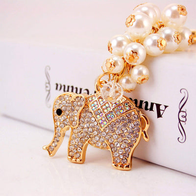 Close-up of a gold-tone elephant charm with an iridescent rhinestone saddle and white pearl-like beads.