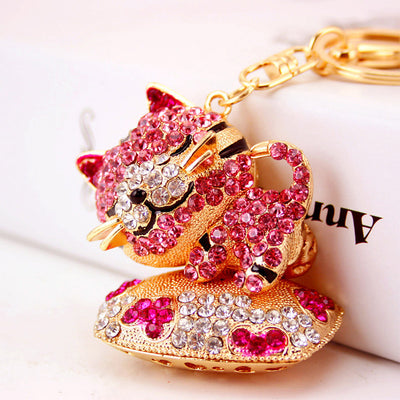 Close-up of a pink rhinestone cat charm resting on a gold-tone decorated cushion.