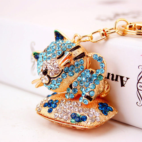 Close-up of a blue rhinestone cat charm with clear stones on its face and cushion.