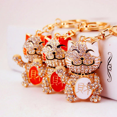 Three clear stone waving cat keychains with white, red, and orange enamel accents.