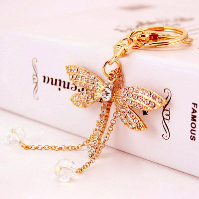 Gold-tone dragonfly keychain with clear stones and two faceted bead dangles resting on a book.