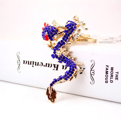 Close-up of a blue rhinestone dragon keychain resting on a white book.