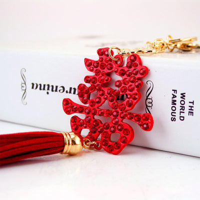 Close-up of a red rhinestone Double Happiness charm and tassel resting against a white book.