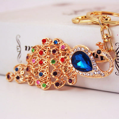 Close-up of a gold-tone peacock keychain with a blue center accent and multicolor tail details.
