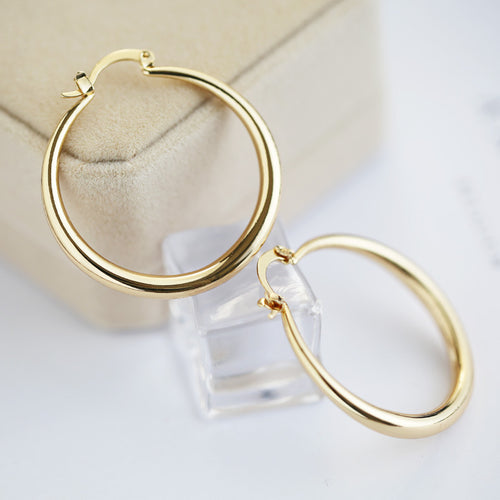 Gold-tone smooth hoops displayed on a pale stand