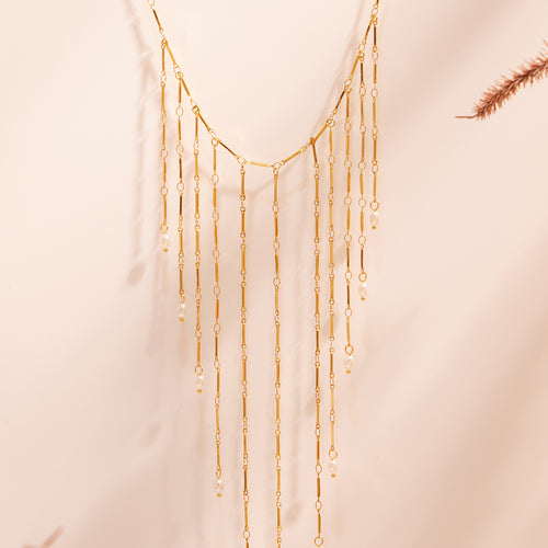 Gold metal fringe necklace hanging against soft backdrop