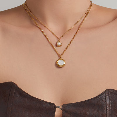 Model wearing layered gold circle mother-of-pearl and heart pearl pendant necklaces