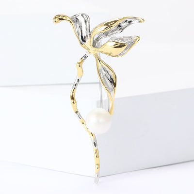 Front view of two-tone leaf branch brooch with white pearl-like bead against a white background.