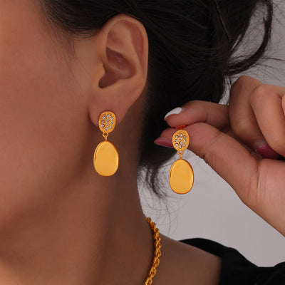 Gold rhinestone oval drop earrings worn on model ear