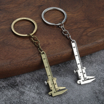 Two mini caliper keychains in silver and antique bronze tones on a wood surface.