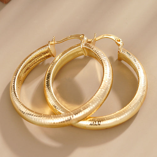 gold tone earrings showing large round hoops with fine horizontal line texture