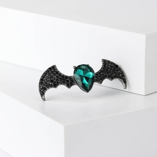 A spread-wing black bat centered by a green heart stone shown in a styled display.
