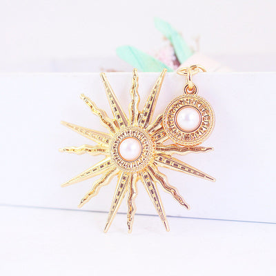 Close-up of a gold-tone sunburst charm and round medallion with white centers.