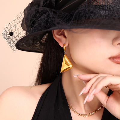 Model in black hat wearing gold 3D triangle pyramid drop earring